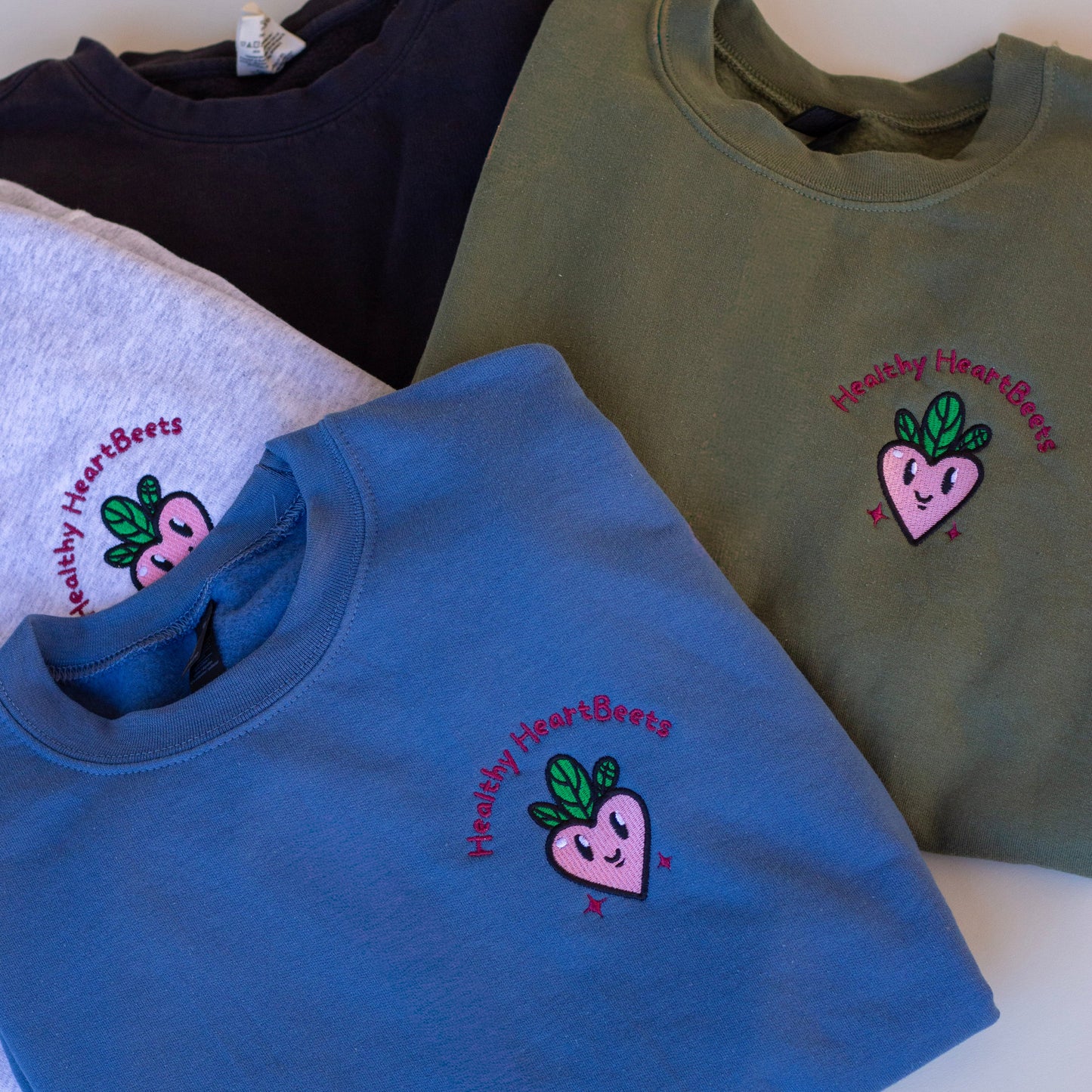 Four sweatshirts in different colors with a logo on a white surface